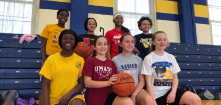 Girls junior high basketball players stand with a basketball in front of the bleachers in the Junior High Gym, with eighth graders in the back row and seventh graders in the front row. The girls’ junior high basketball teams have games throughout the week.