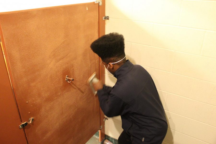 Micah Ballard, ‘21, vigorously sands the inside of a stall in preparation for decorating. Art club members hope this will not only beautify the school, but also discourage vandalism.