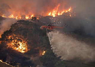 In this Monday, Dec. 30, 2019 photo provided by State Government of Victoria, a helicopter tackles a wildfire in East Gippsland, Victoria state, Australia. Wildfires burning across Australias two most-populous states trapped residents of a seaside town in apocalyptic conditions Tuesday, Dec. 31, and were feared to have destroyed many properties and caused fatalities. (State Government of Victoria via AP)