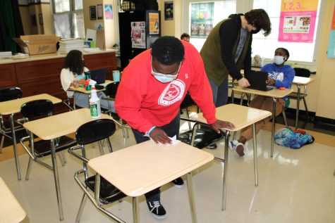 Alonzo Montgomery ‘23, exhibiting covid protocol procedures, by cleaning off the desks of his classroom.