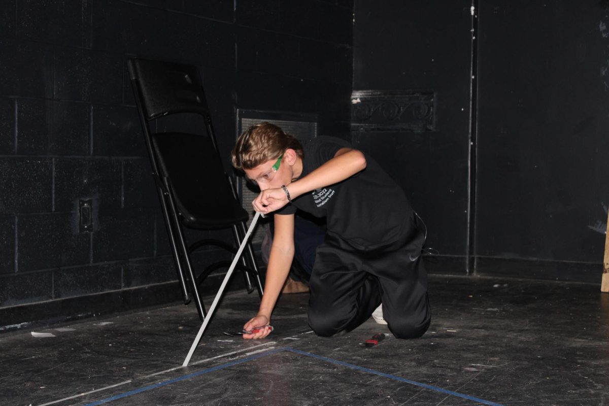 Jonas Warner, ‘27 prepares the black box theater for the Laramie Project by removing tape and clearing the stage.